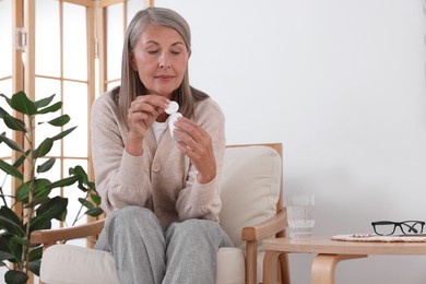 Senior woman with bottle of pills in armchair at home