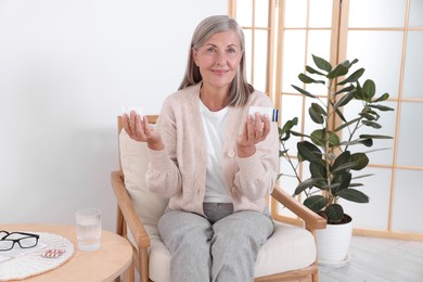 Photo of Senior woman with bottles of pills in armchair at home