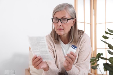 Photo of Senior woman with pills reading medicine instruction at home