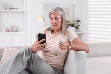 Senior woman with pills using smartphone on sofa at home