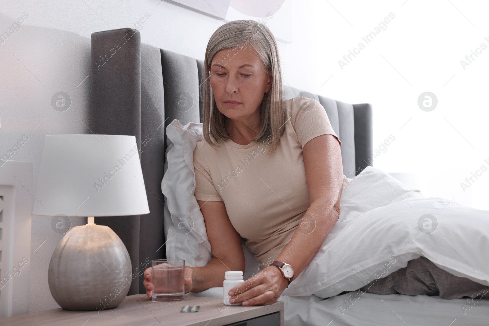 Photo of Senior woman taking pill bottle in bed at home