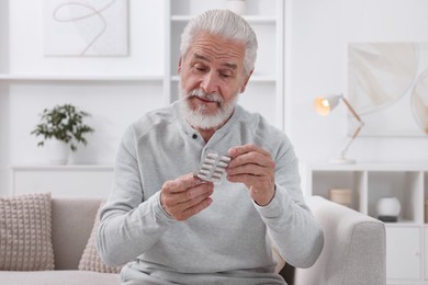 Photo of Senior man holding blister with pills at home