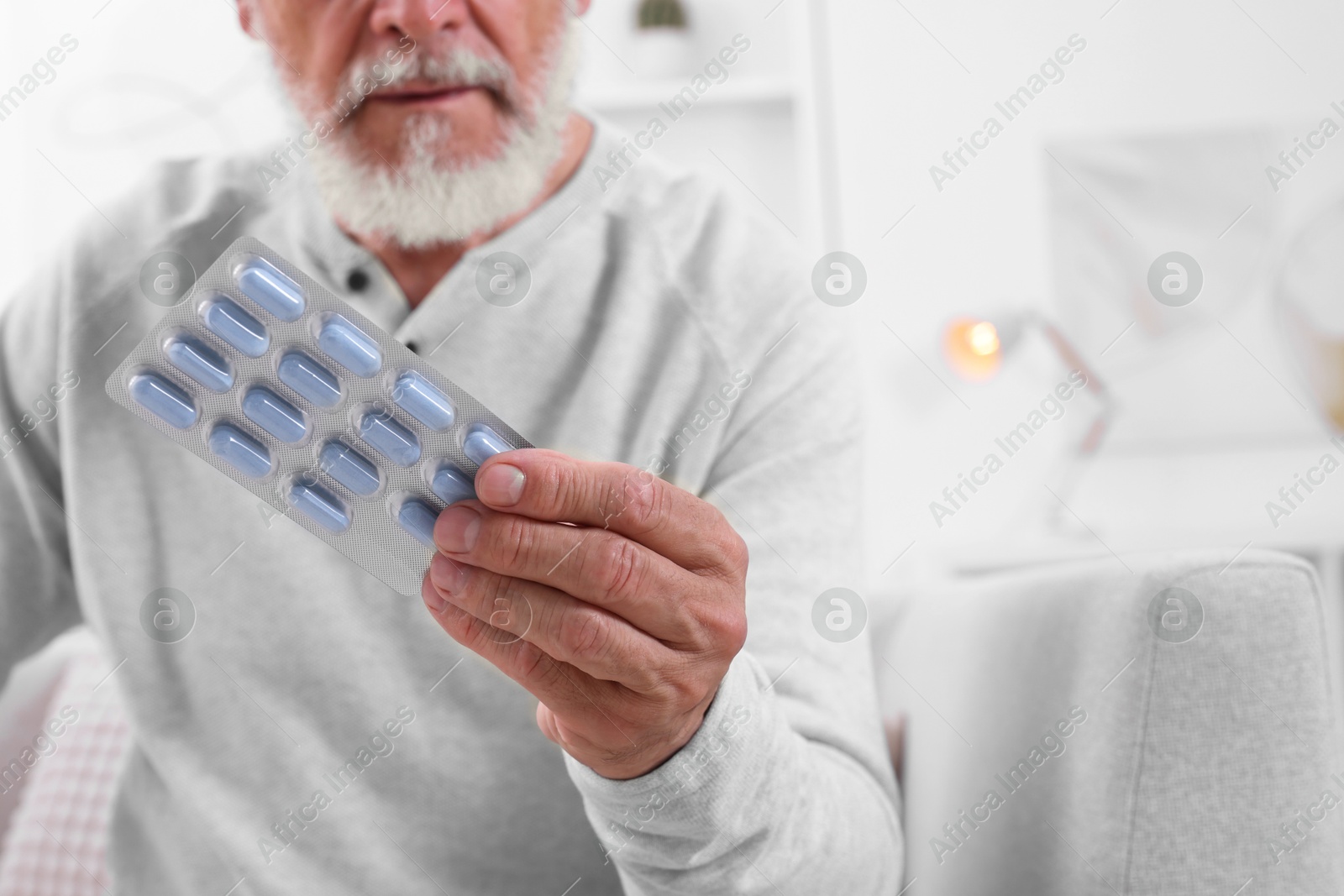 Photo of Senior man holding blister with pills at home, closeup