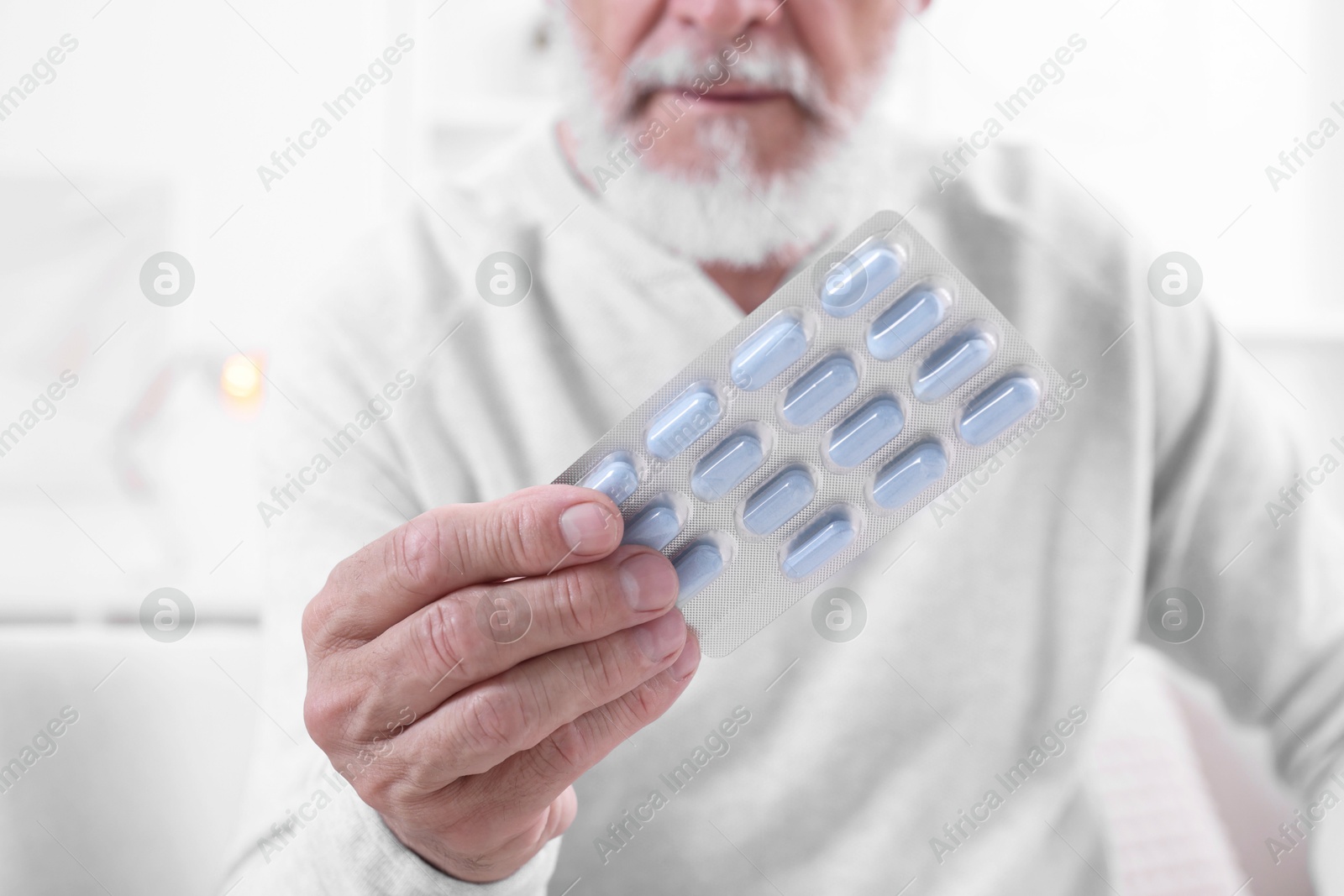 Photo of Senior man holding blister with pills at home, closeup