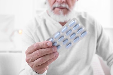 Photo of Senior man holding blister with pills at home, closeup