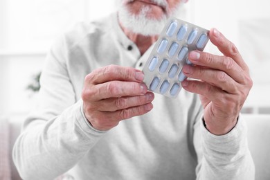 Senior man holding blister with pills at home, closeup