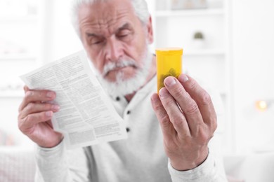 Photo of Senior man with pills reading medicine instruction at home, selective focus