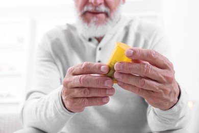 Senior man holding bottle with pills at home, closeup