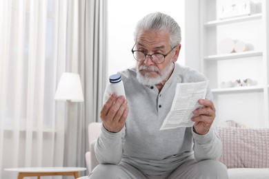 Senior man with pill bottle and medicine instruction on sofa at home