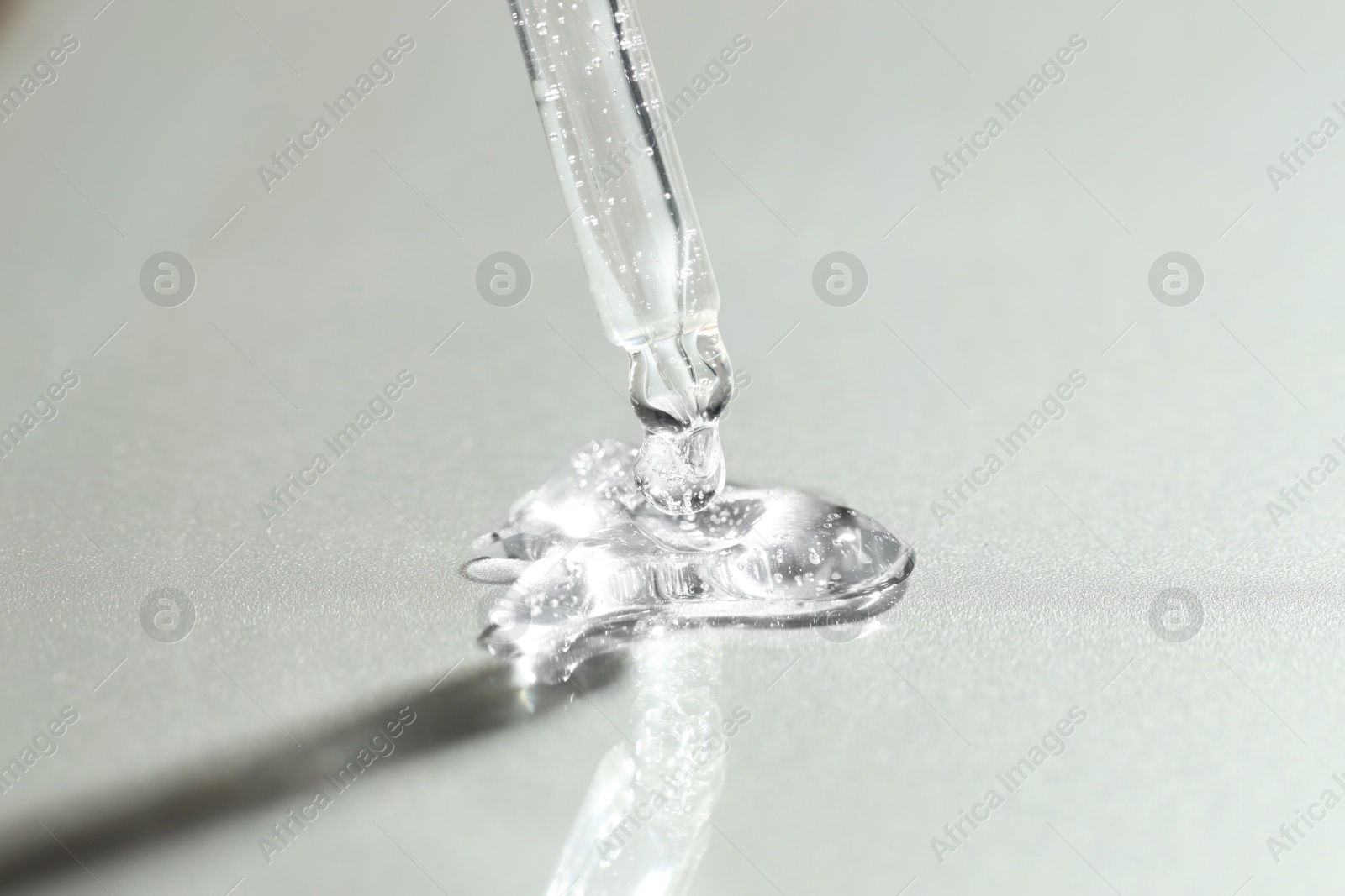 Photo of Dripping cosmetic serum from pipette on grey background, closeup