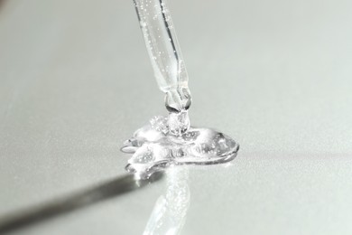 Photo of Dripping cosmetic serum from pipette on grey background, closeup