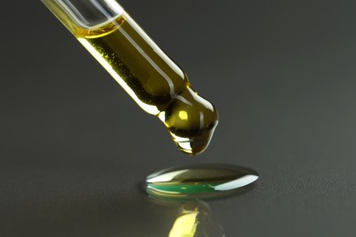 Photo of Dripping essential oil from pipette on grey background, closeup