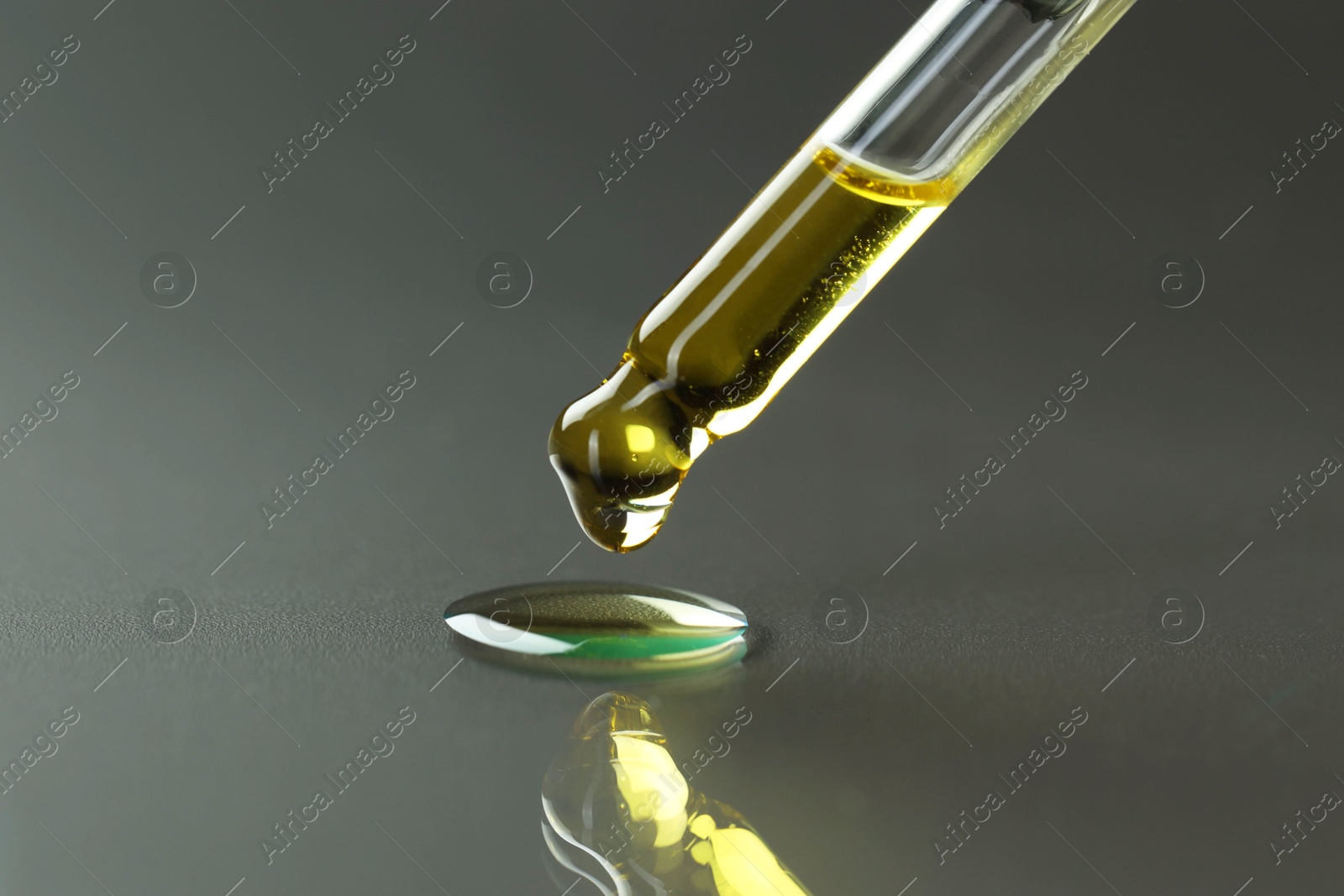 Photo of Dripping essential oil from pipette on grey background, closeup