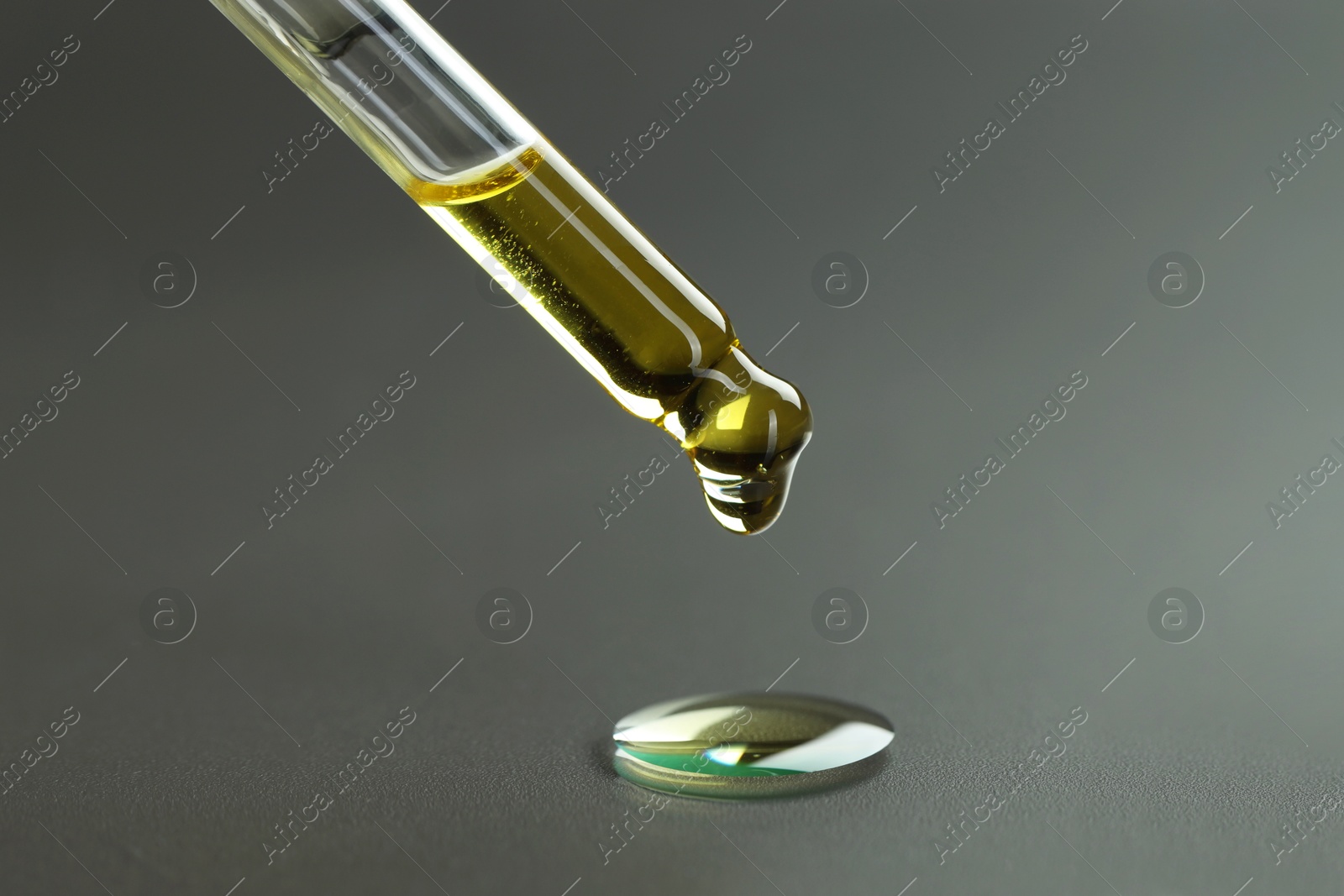 Photo of Dripping essential oil from pipette on grey background, closeup