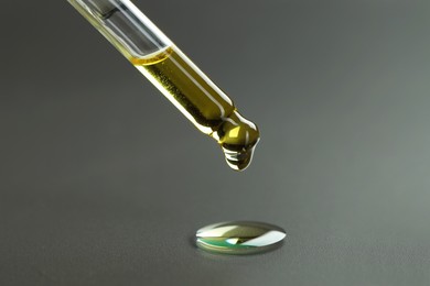 Photo of Dripping essential oil from pipette on grey background, closeup