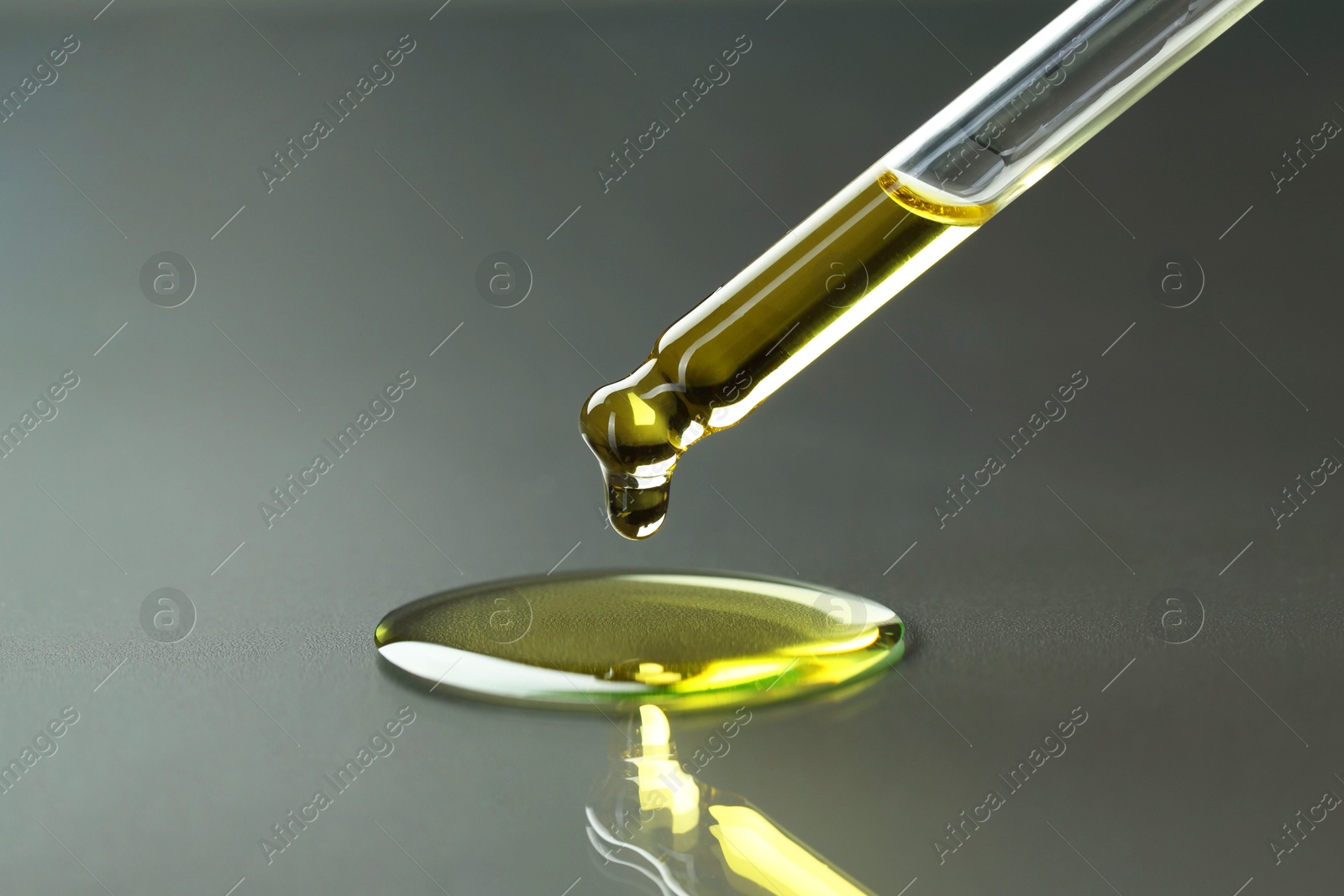 Photo of Dripping essential oil from pipette on grey background, closeup