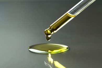 Photo of Dripping essential oil from pipette on grey background, closeup