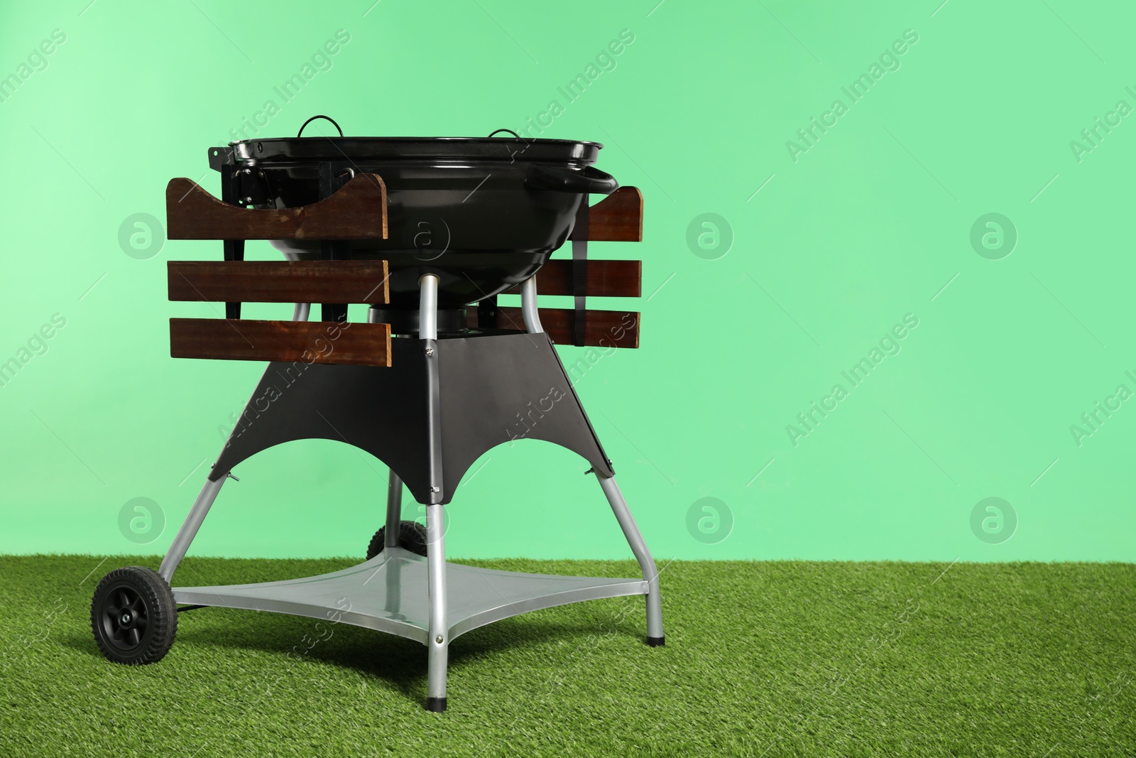 Photo of One black barbeque grill on grass against green background. Space for text