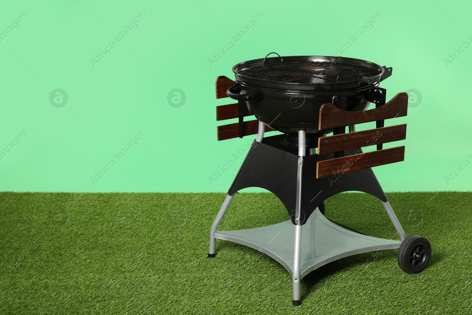 Photo of One black barbeque grill on grass against green background. Space for text