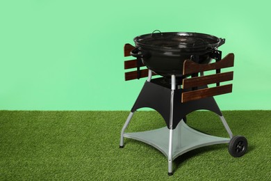 Photo of One black barbeque grill on grass against green background. Space for text