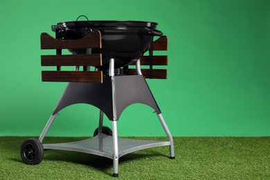 Photo of One black barbeque grill on grass against green background. Space for text