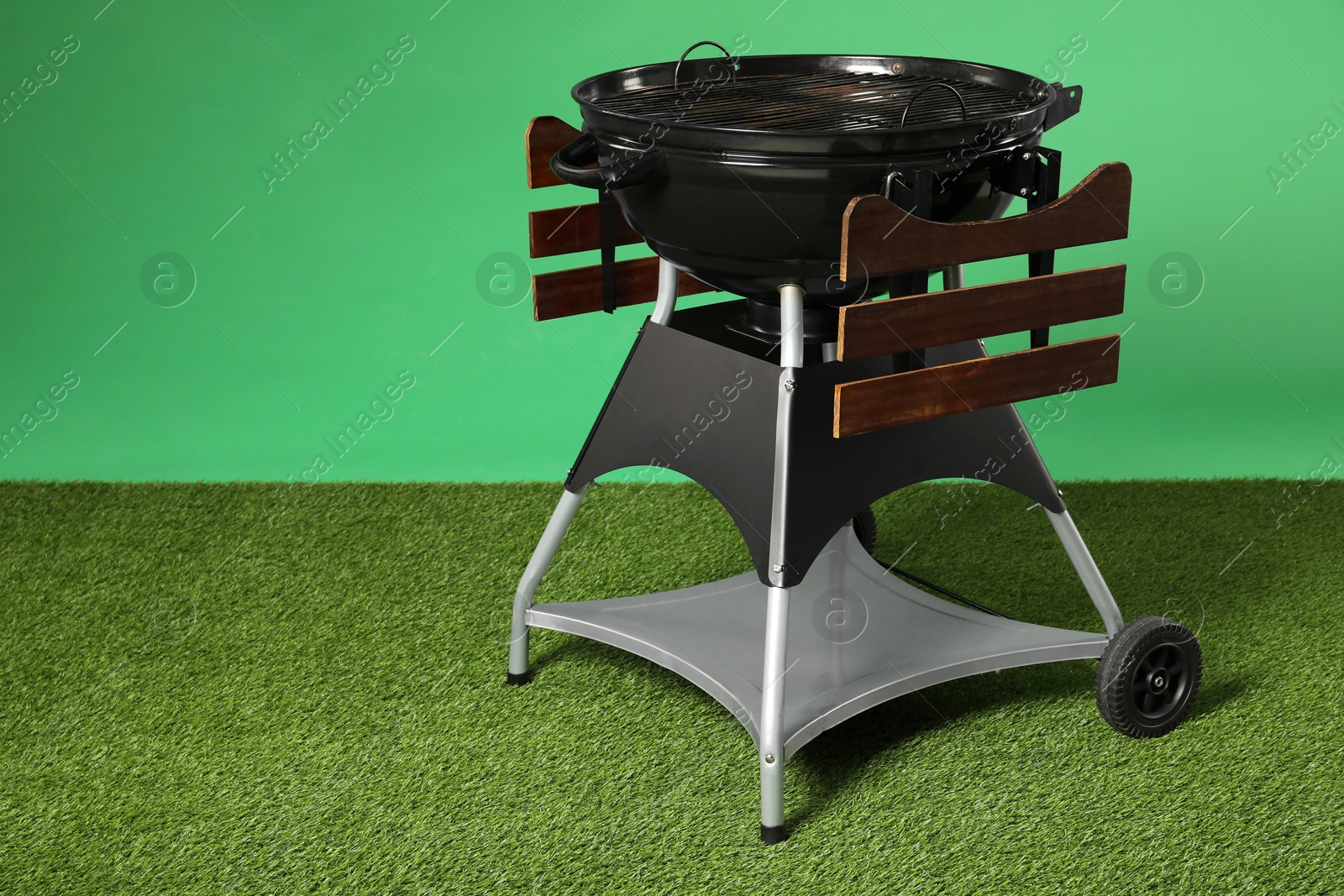 Photo of One black barbeque grill on grass against green background. Space for text