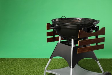 Photo of One black barbeque grill on grass against green background. Space for text