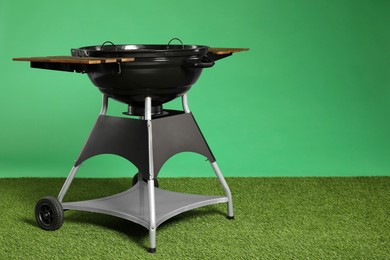 Photo of One black barbeque grill on grass against green background. Space for text