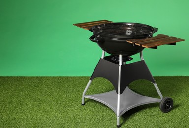 Photo of One black barbeque grill on grass against green background. Space for text