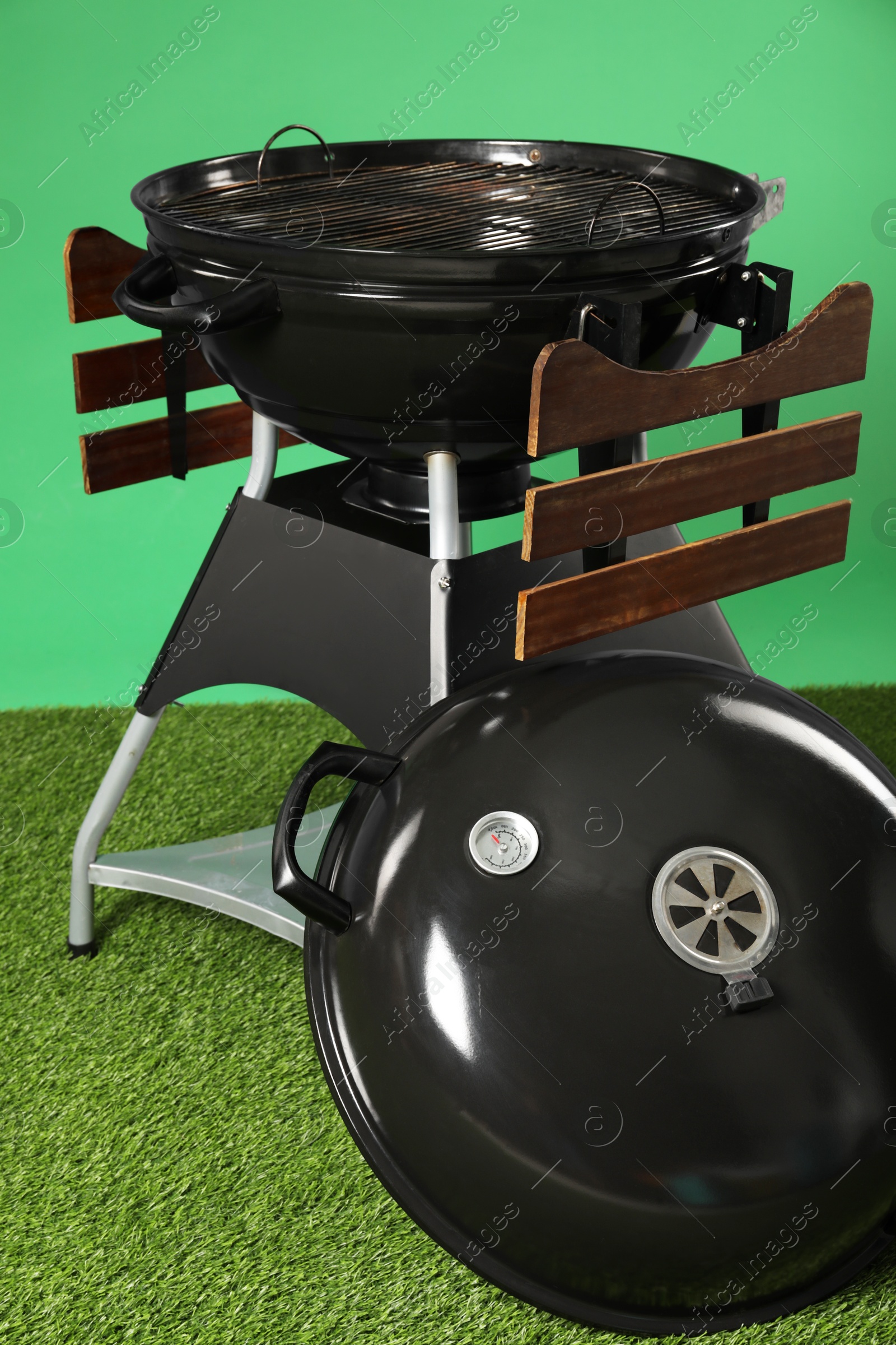 Photo of One black barbeque grill on grass against green background. Cooking appliance