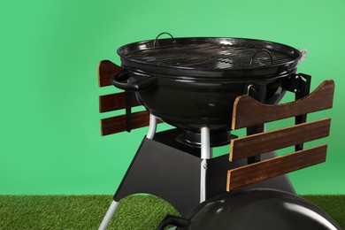 Photo of One black barbeque grill on grass against green background. Space for text