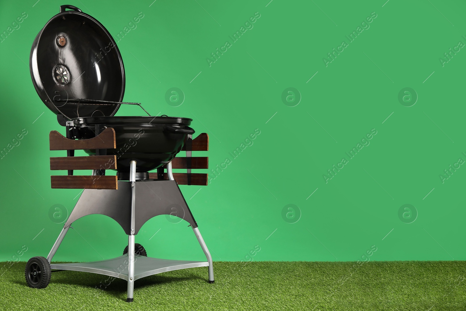 Photo of One black barbeque grill on grass against green background. Space for text