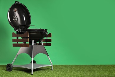 Photo of One black barbeque grill on grass against green background. Space for text