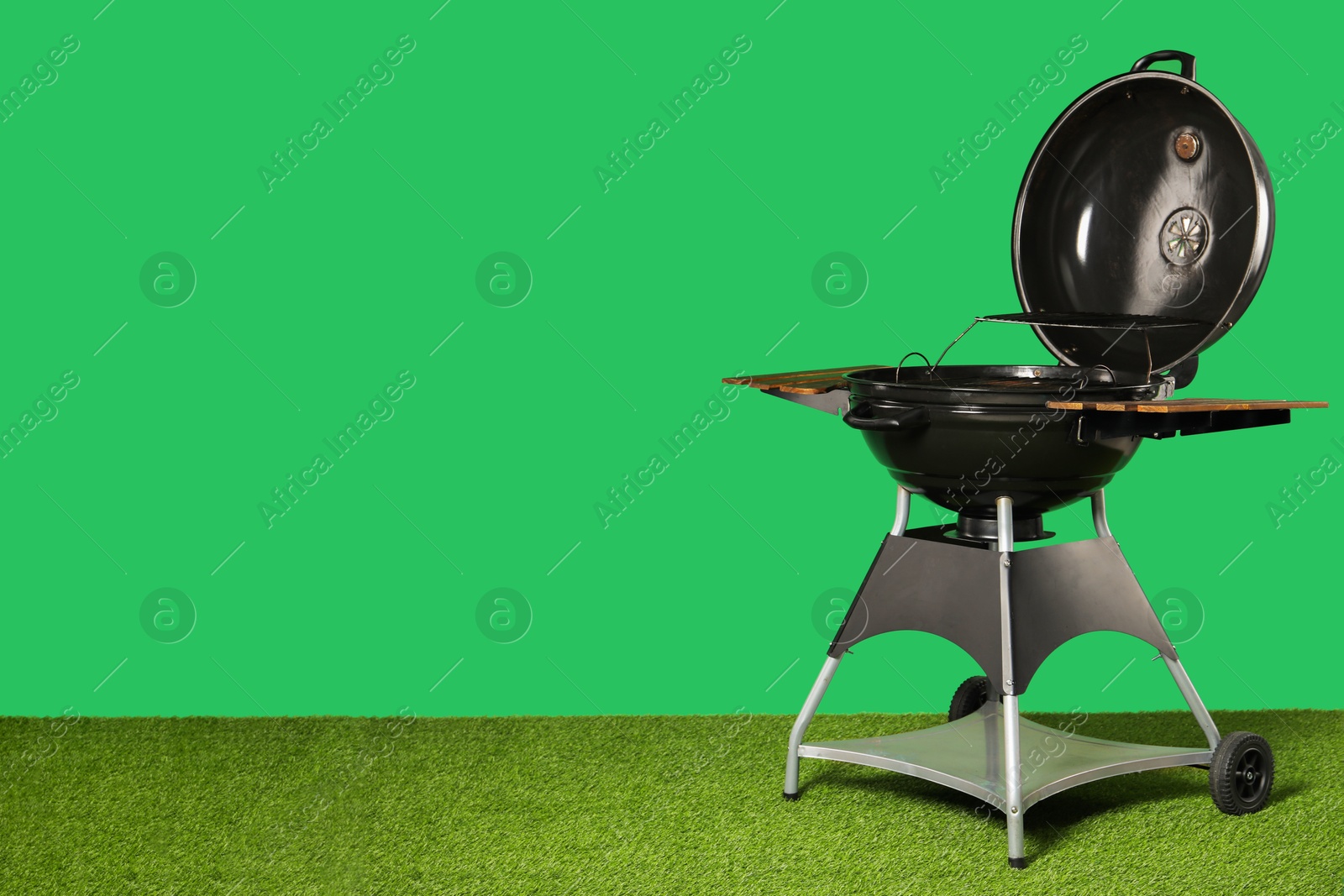 Photo of One black barbeque grill on grass against green background. Space for text