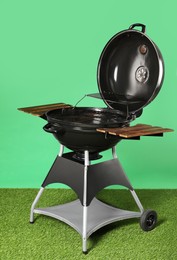 Photo of One black barbeque grill on grass against green background