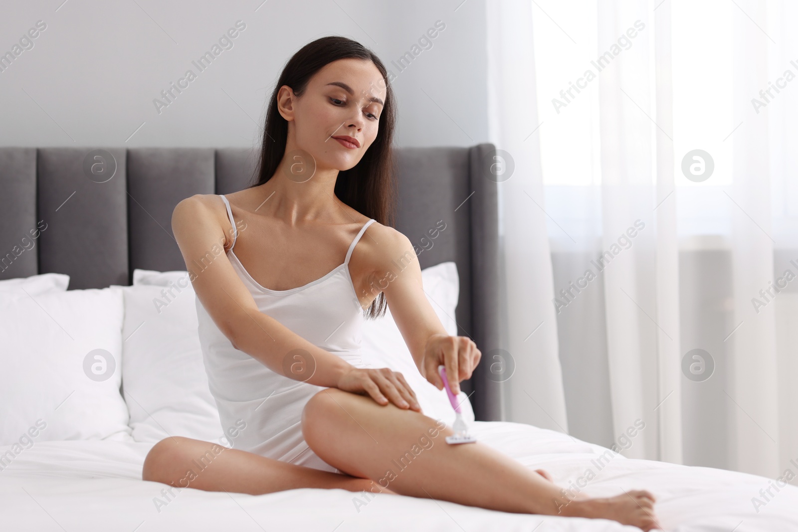 Photo of Beautiful woman shaving leg on bed at home