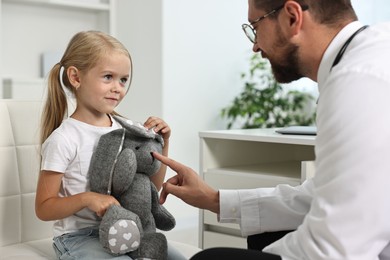 Photo of Little girl with toy having appointment with doctor in hospital