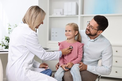 Doctor examining little girl with stethoscope and her father in hospital