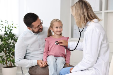 Photo of Doctor examining little girl with stethoscope and her father in hospital