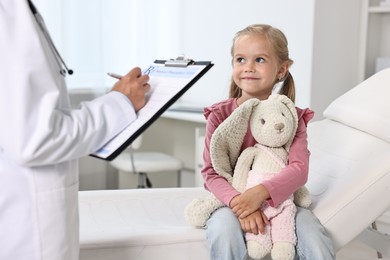 Doctor consulting little girl with toy in hospital, closeup