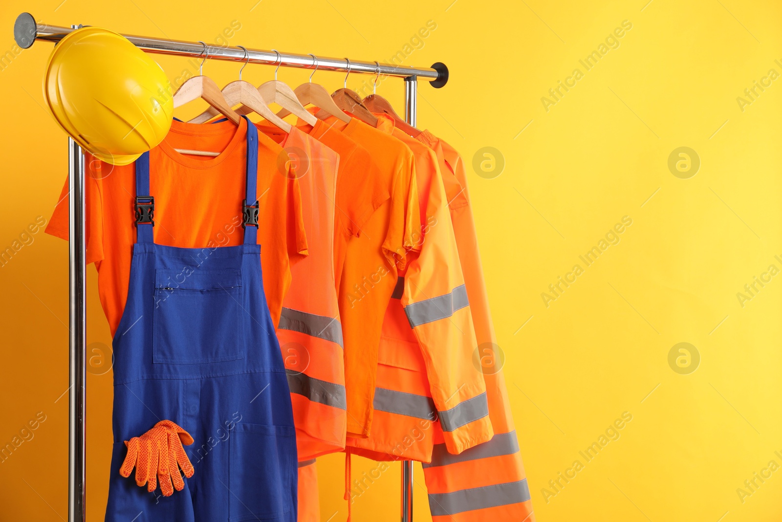 Photo of Workers' uniforms on clothing rack against yellow background. Space for text