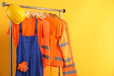 Photo of Workers' uniforms on clothing rack against yellow background. Space for text