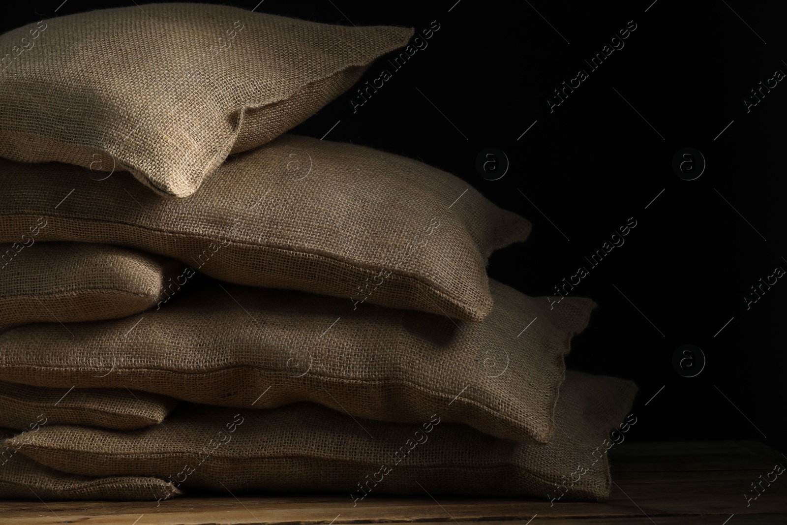 Photo of Group of burlap sacks on wooden table against black background