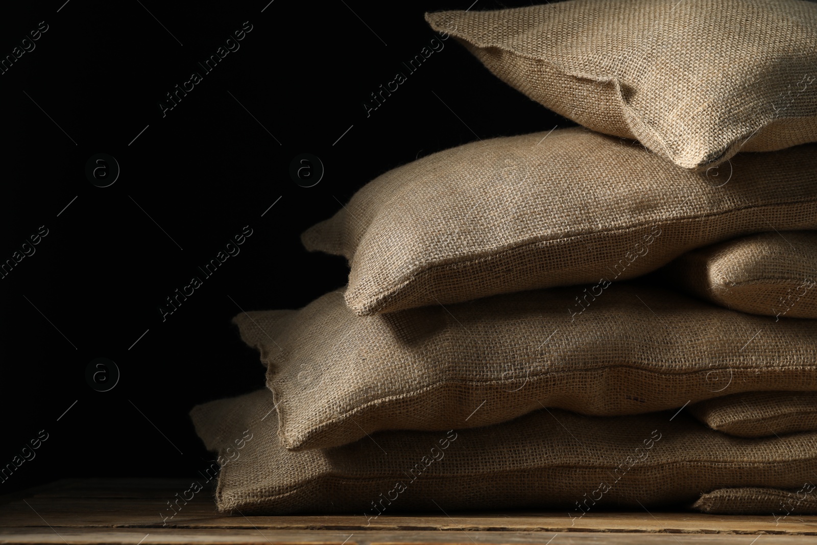 Photo of Group of burlap sacks on wooden table against black background, space for text