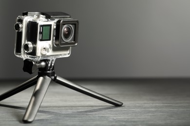 Modern action camera and tripod on grey wooden table. Space for text