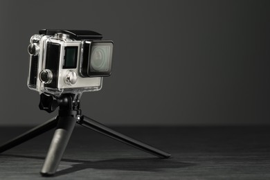 Modern action camera and tripod on grey wooden table. Space for text