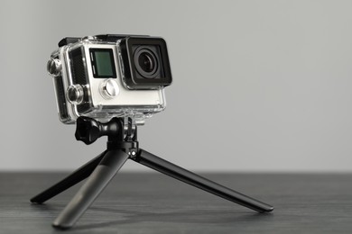 Photo of Modern action camera and tripod on wooden table against grey background