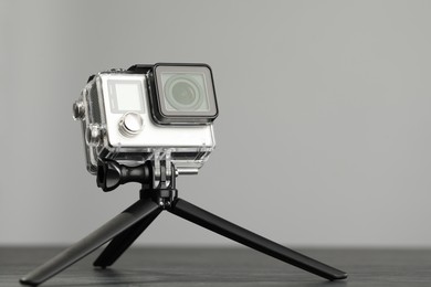 Modern action camera and tripod on wooden table against grey background. Space for text