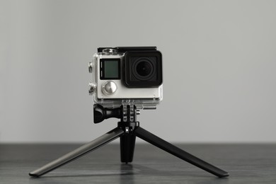 Photo of Modern action camera and tripod on wooden table against grey background