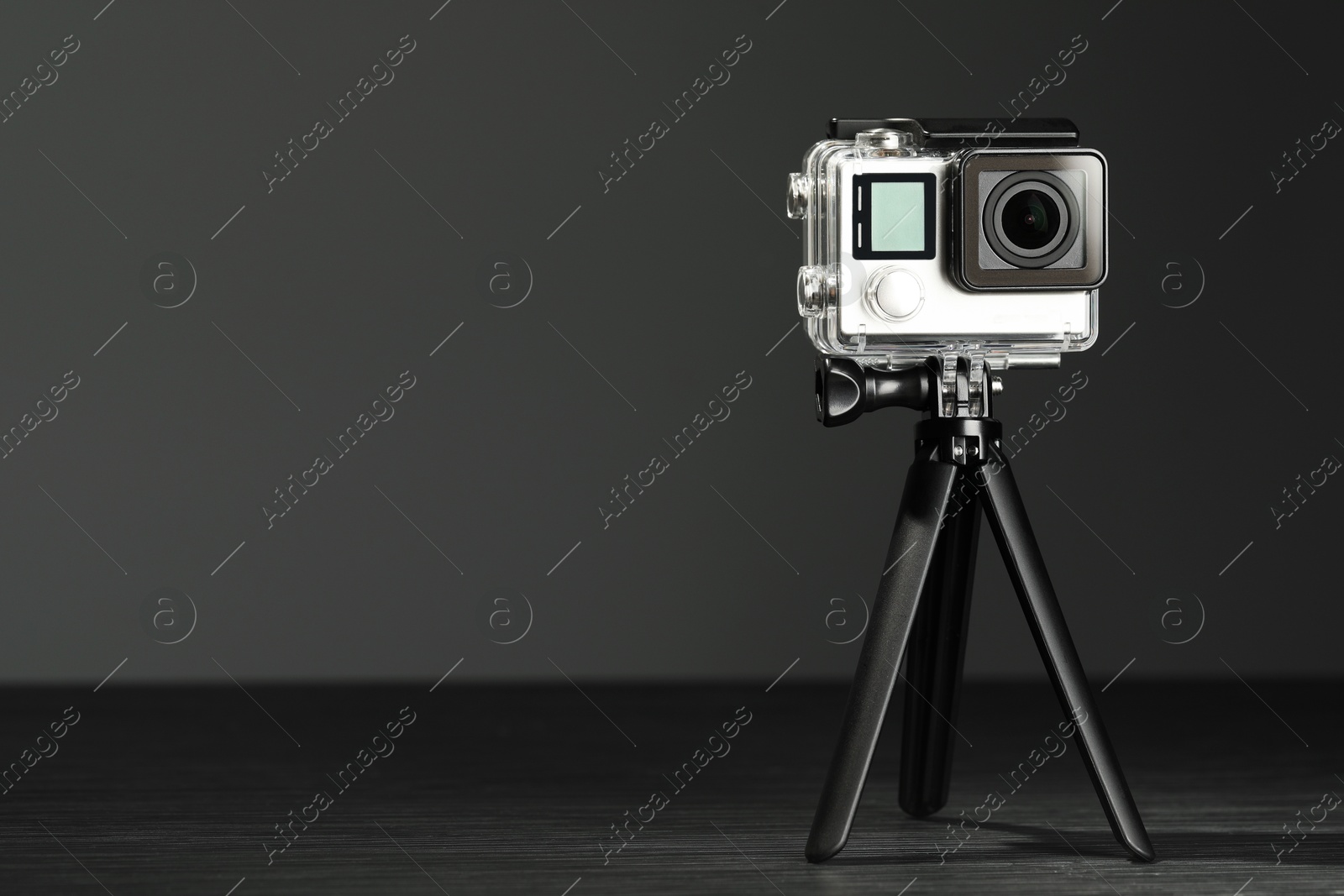 Photo of Modern action camera and tripod on grey wooden table. Space for text